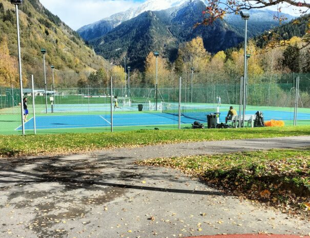 Terrain de tennis extérieur à Bozel, entouré de montagnes et accessible sur réservation.